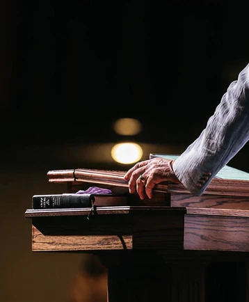 A hand resting on a wooden pulpit beside an open Bible